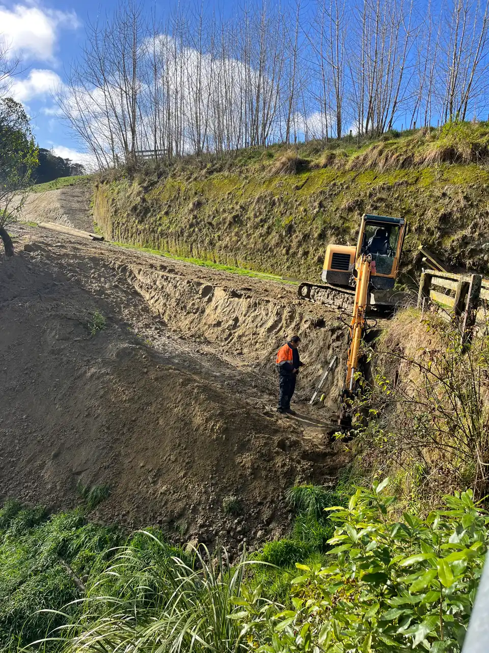 Excavator benching a road bank with a worker checking levels