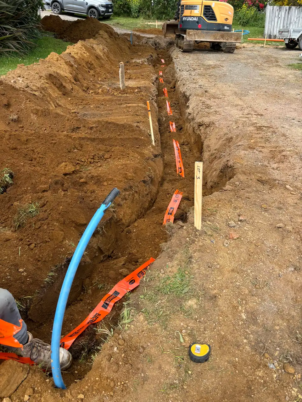 Trench with blue water pipe and orange warning tape laid out